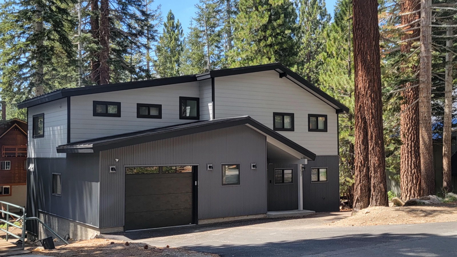 Modern mountain home with a black standing-seam roof, white lap siding and corrugated grey metal, built among tall pines